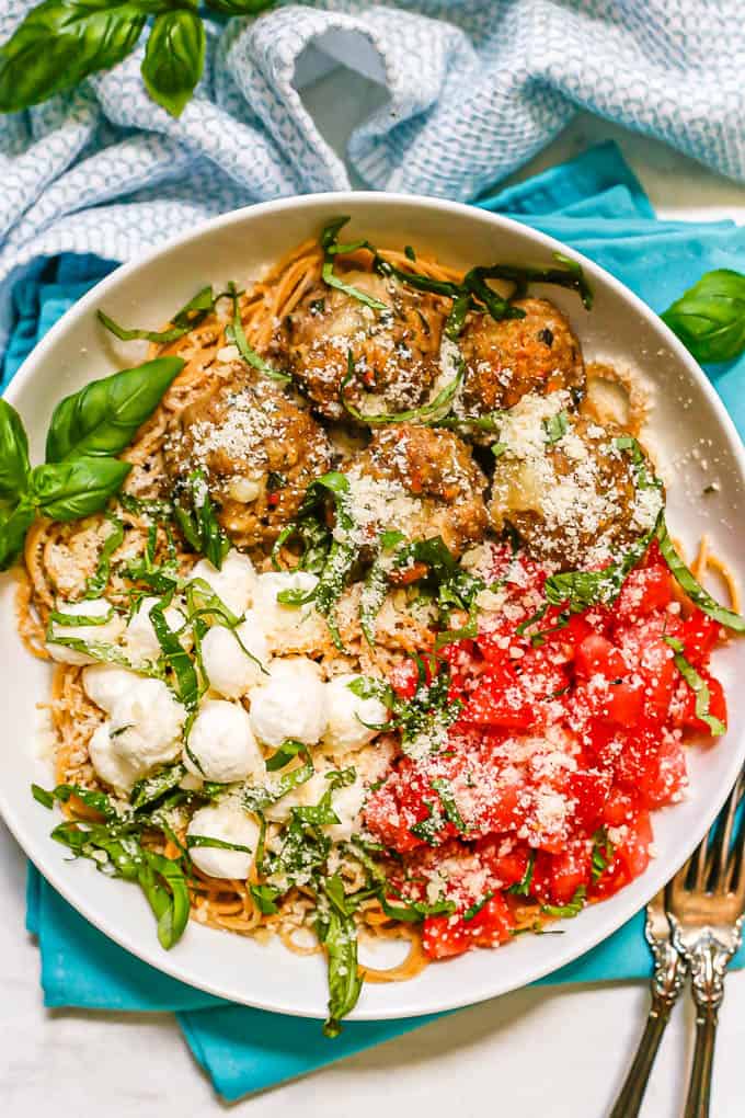 Caprese meatballs served over spaghetti in a low white bowl with fresh tomatoes, mozzarella, basil and Parmesan
