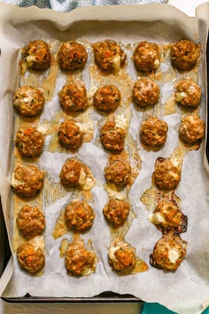 Meatballs on a parchment paper lined baking sheet after coming out of the oven