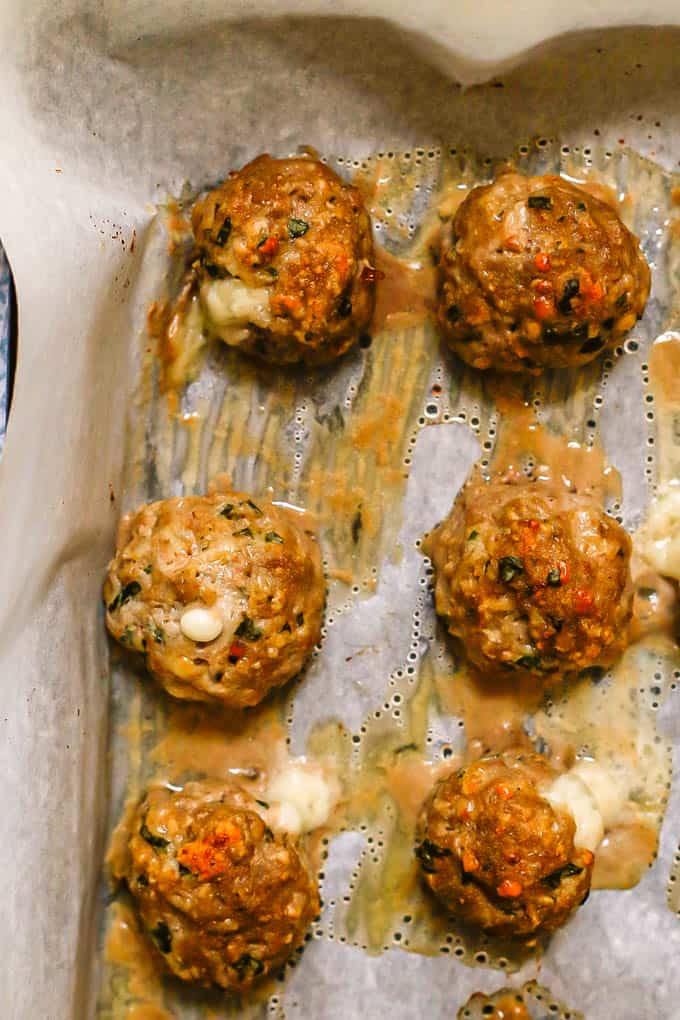 Close up of baked turkey meatballs with mozzarella in the middle on a parchment paper lined baking sheet