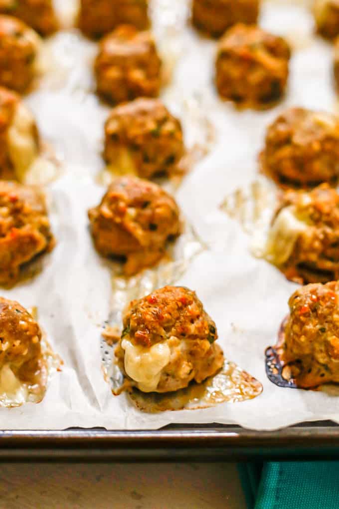 Baked meatballs with cheese oozing out on a parchment paper lined baking sheet