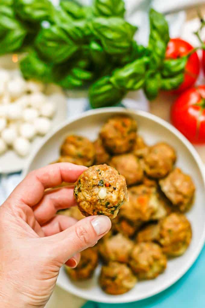 A hand holding up a baked turkey meatball with mozzarella in the center