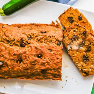 A loaf of chocolate chip zucchini bread with a couple of pieces sliced on a white plate