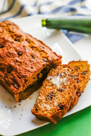Chocolate chip zucchini bread on a large rectangular white plate with a couple of pieces sliced and topped with butter