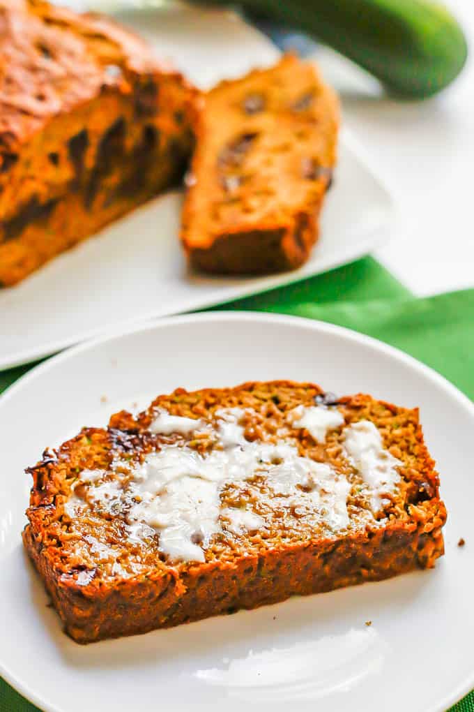 A sliced of buttered chocolate chip zucchini bread on a white plate set on green napkins
