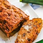 Chocolate chip zucchini bread on a large rectangular white plate with a couple of pieces sliced and topped with butter and a text overlay on the photo