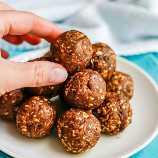 Chocolate peanut butter energy balls piled in a pyramid on a small white plate with a hand reaching for the top one