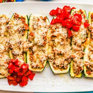 Halved zucchini boats with a turkey sausage stuffing and melted cheese on top served on a white rectangular plate