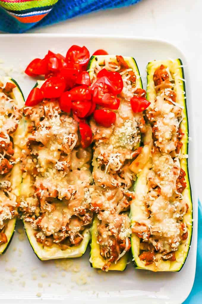 Close up of cheese and turkey sausage stuffed zucchini topped with chopped fresh tomatoes on a white serving plate