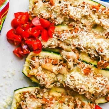 Baked stuffed zucchini served on a white plate with chopped fresh tomatoes on top