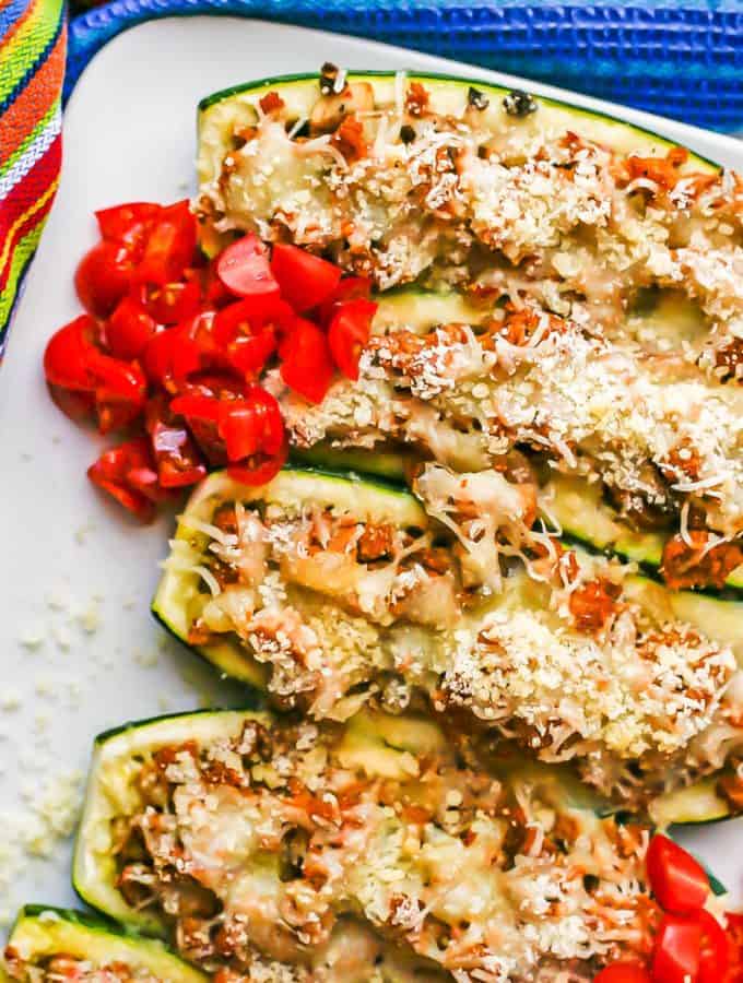Baked stuffed zucchini served on a white plate with chopped fresh tomatoes on top