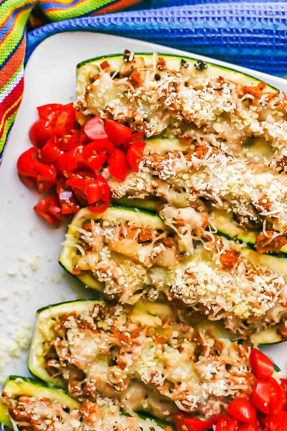 Baked stuffed zucchini served on a white plate with chopped fresh tomatoes on top