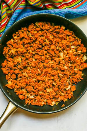 Crumbled, cooked turkey sausage with onions and mushrooms in a large dark skillet