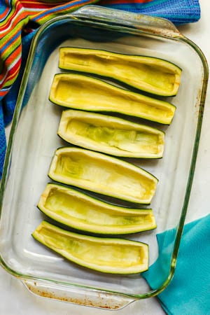 Hulled out zucchini boats in a glass baking dish before being stuffed