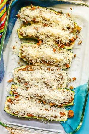 Zucchini boats in a glass baking dish stuffed with a turkey sausage mixture and topped with cheese before being baked