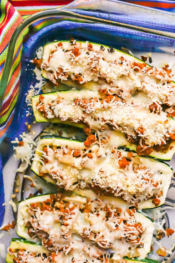 Close up of sausage stuffed zucchini boats in a glass baking dish with melty cheese on top