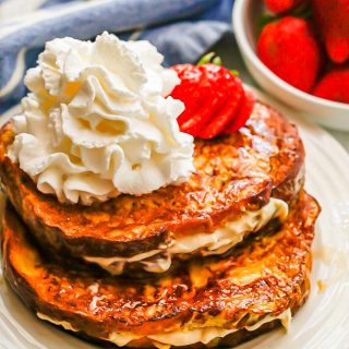Stuffed French toast on a white plate topped with strawberries and whipped cream