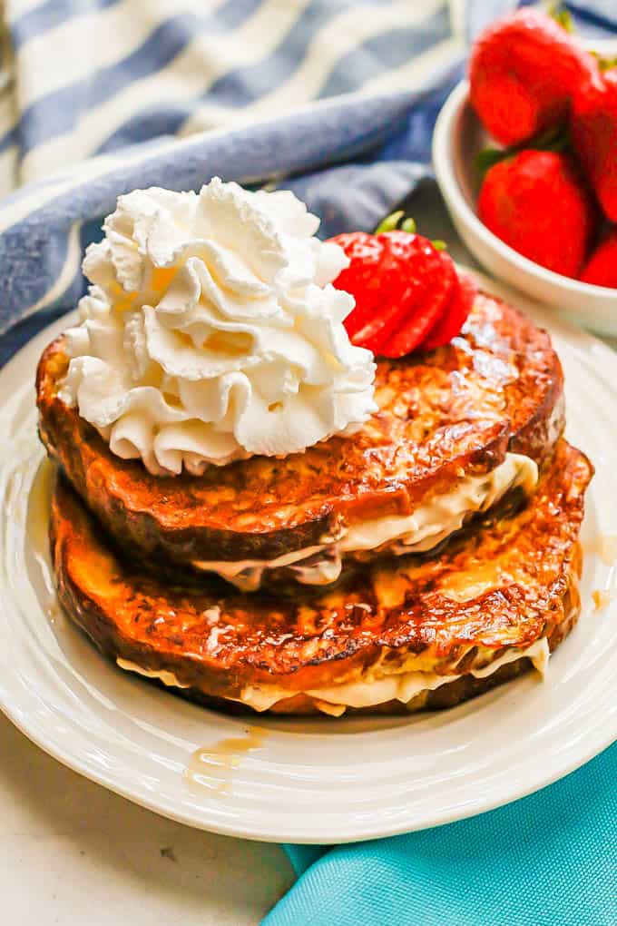 Two pieces of French toast stuffed with a cream cheese mixture and topped with strawberries and whipped cream