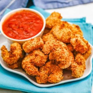 A white serving plate with crispy breaded shrimp and a small bowl of marinara sauce