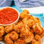 Close up of crispy Air Fryer breaded shrimp served on a white plate with a bowl of marinara with a text overlay on the photo