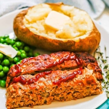 Ground turkey meatloaf slices served on a white plate with a baked potato and green peas