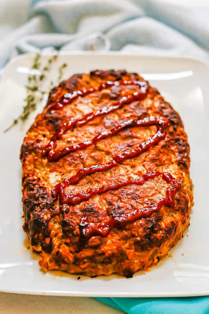 Side angle view of a browned and baked turkey meatloaf with ketchup on top on a white plate