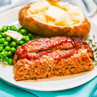 A white dinner plate with a baked potato, green peas and two slices of turkey meatloaf