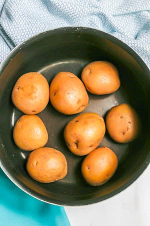 Whole Yukon potatoes in a large dark pot before being cooked