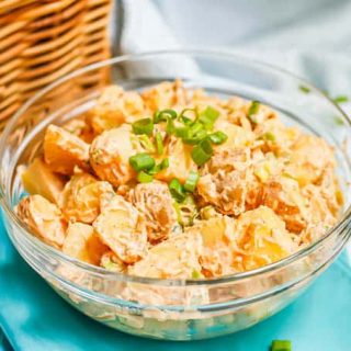 A bowl full of healthy potato salad set on aqua napkins with a picnic basket in the background