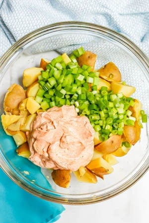 Ingredients for potato salad layered together in a large glass bowl before being mixed