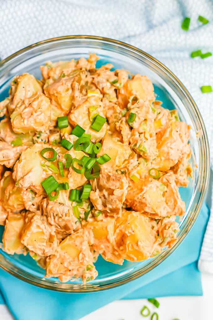 Overhead close up look at potato salad in a glass bowl with sliced green onions sprinkled on top and scattered to the side