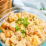 A glass bowl with a creamy potato salad topped with sliced green onions and a text box overlay on the photo