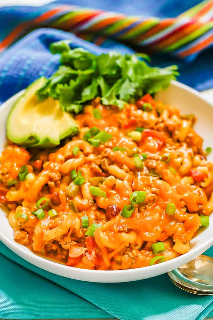 Cheesy turkey chili mac served in a low white bowl with sliced avocado and cilantro to the side