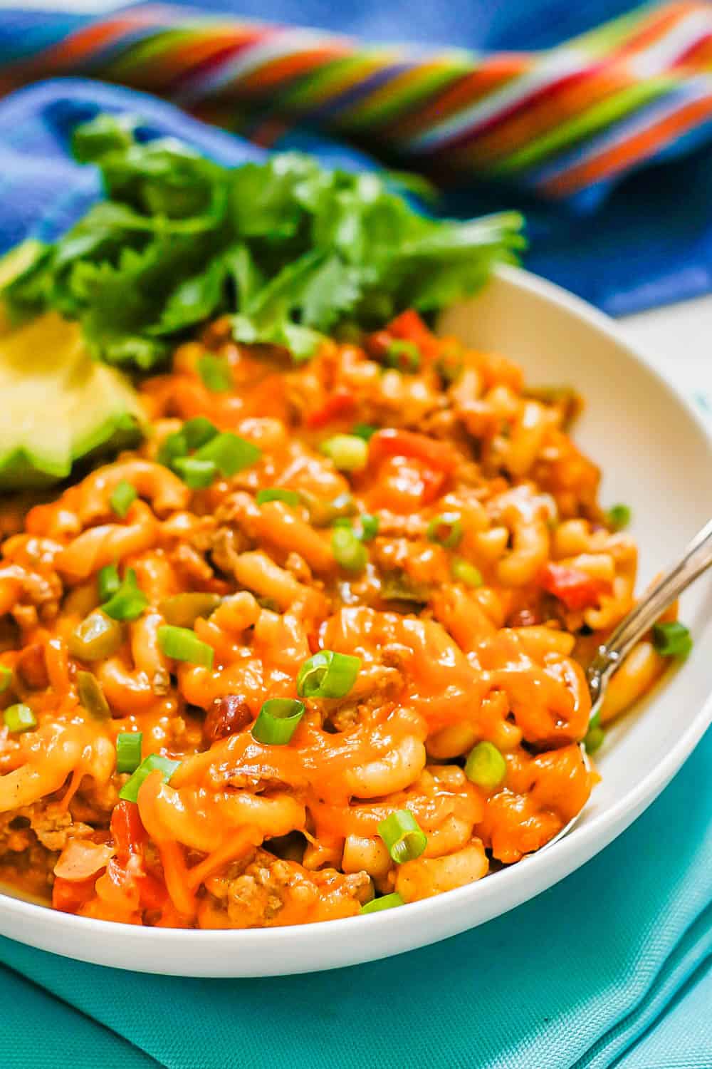 A fork resting in a low white bowl of cheesy one pot turkey chili mac set on teal napkins