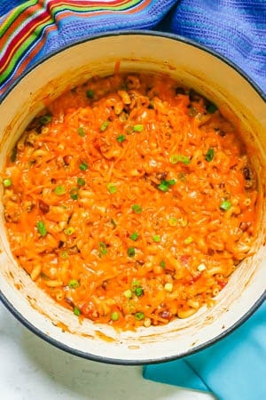 Turkey chili mac in a large Dutch oven with a layer of melted cheddar cheese on top and a sprinkling of sliced green onions