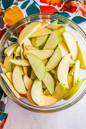 A glass bowl filled with thinly sliced green and red apples