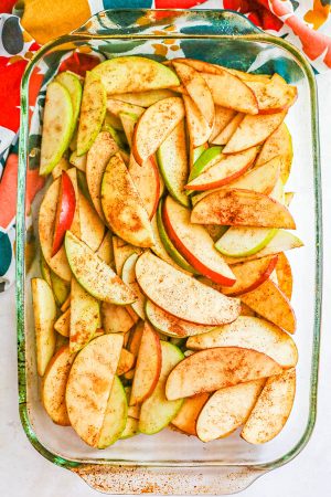 A glass baking dish filled with sliced green and red apples sprinkled with cinnamon