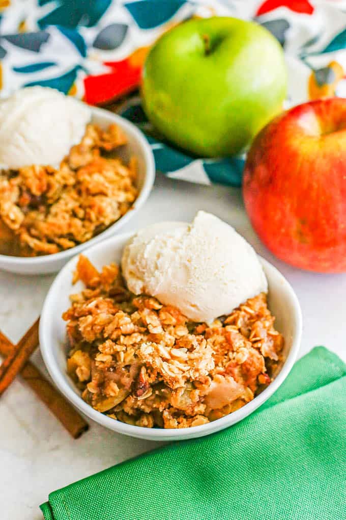 Close up of a low white bowl with apple crisp with a streusel topping and a small scoop of vanilla