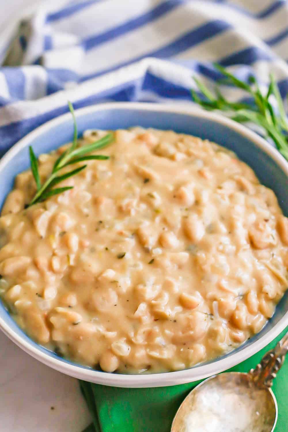 Creamy white beans served in a blue and white bowl with a sprig of rosemary for garnish