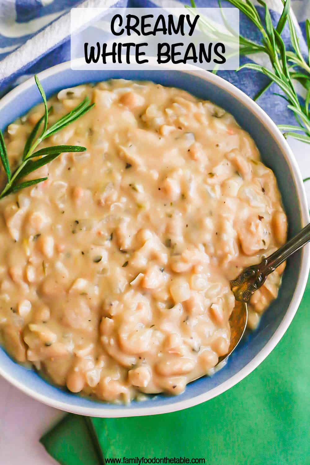 A spoon resting in a blue and white bowl of creamy white beans with rosemary sprigs to the side and a text overlay on the photo