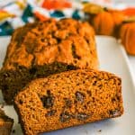Close up of a slice of pumpkin bread with chocolate chips sliced on a white plate with a text overlay on the photo