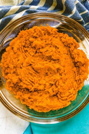 A clear bowl with mashed sweet potatoes and blue and turquoise napkins nearby