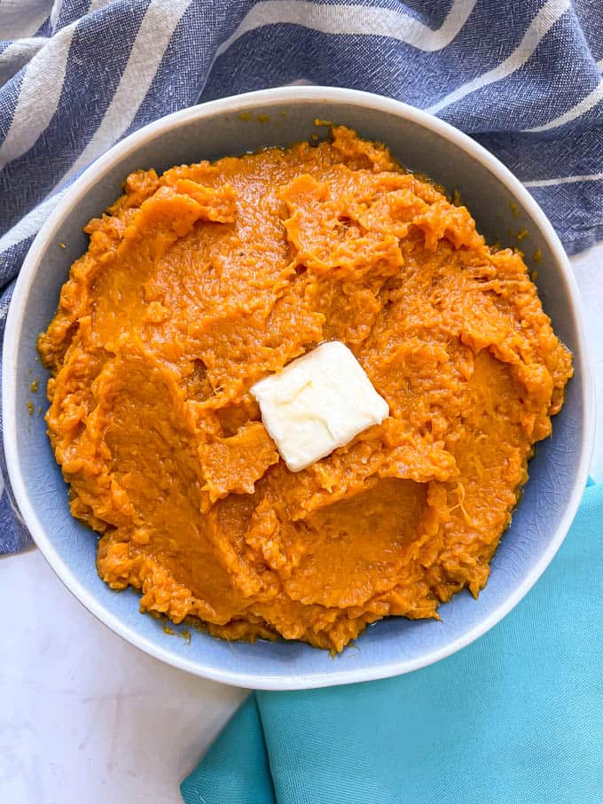 Creamy mashed sweet potatoes in a blue and white bowl with a pat of butter on top