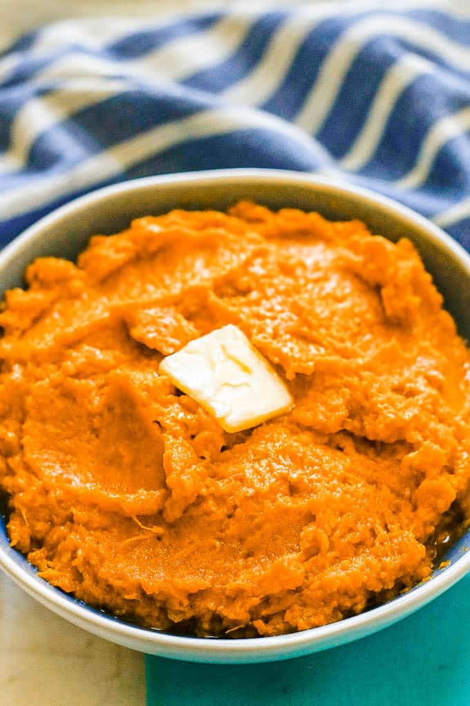 A blue and white serving bowl with mashed sweet potatoes with a pat of butter on top