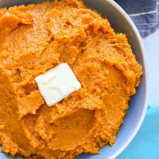 Close up of creamy mashed sweet potatoes in a blue serving bowl with a pat of butter on top