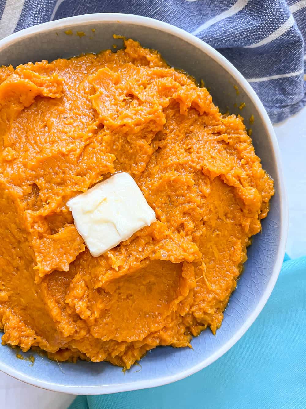 Close up of creamy mashed sweet potatoes in a blue serving bowl with a pat of butter on top