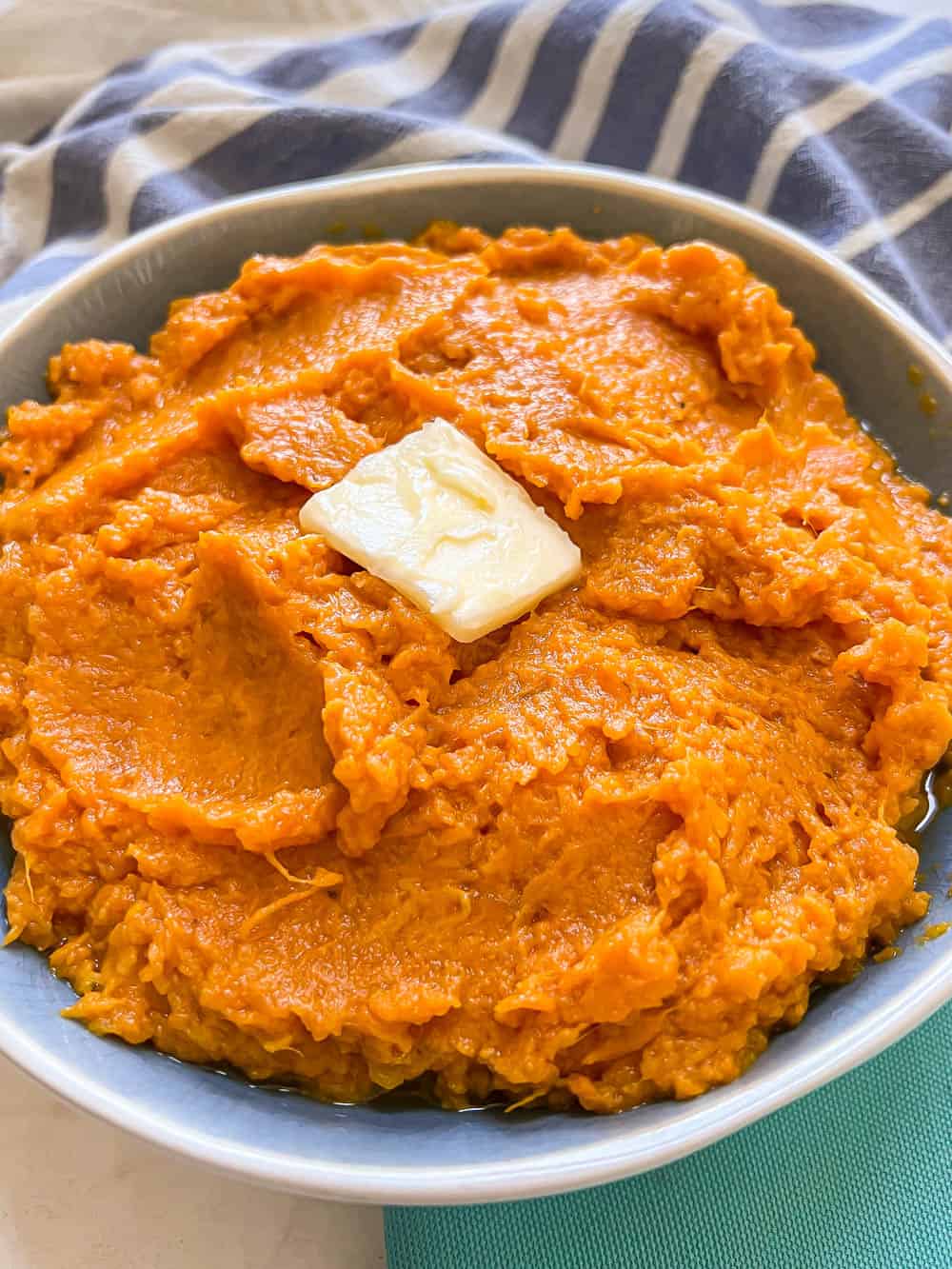 Mashed sweet potatoes with a pat of butter in a blue and white bowl set on teal napkins