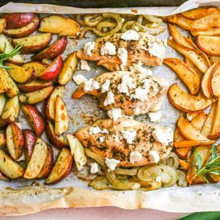 A sheet pan with roasted chicken, potatoes, onions and apples and sprigs of rosemary