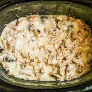 Shredded chicken in a creamy sauce with melted mozzarella cheese on top in a crock pot