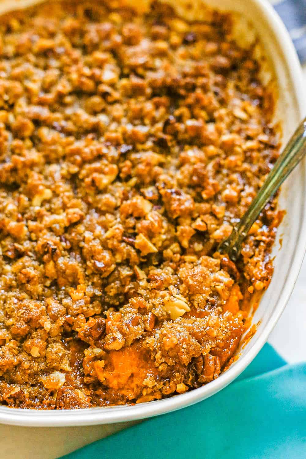 A silver serving spoon scooping out sweet potato casserole with a pecan streusel topping from a white baking dish