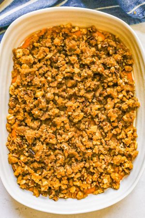 Sweet potato casserole with a pecan topping in a white baking dish before being baked